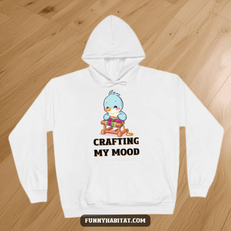 Funny bird character arranging colorful yarn on a tiny loom, a warm and humorous hoodie for crafters.